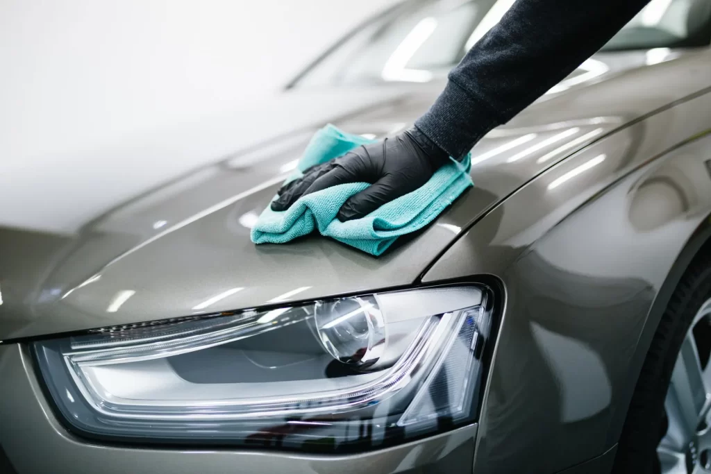 Processus de détail automobile en cours, avec un professionnel nettoyant le capot gris d'une voiture avec un chiffon en microfibre turquoise pour un fini impeccable.