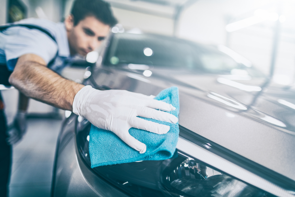 Spécialiste en soins auto utilisant de l'eau chaude savonneuse pour enlever des taches de sève sur une voiture.