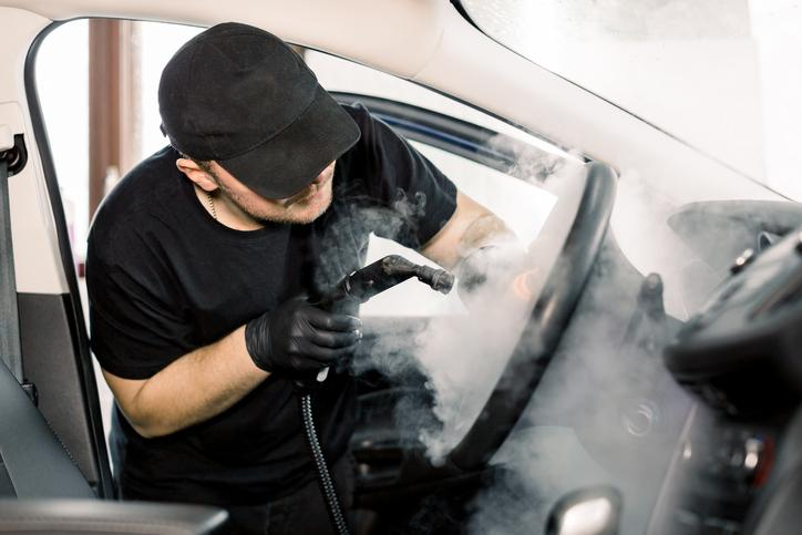 Technicien en esthétique automobile avec nettoyeur vapeur.