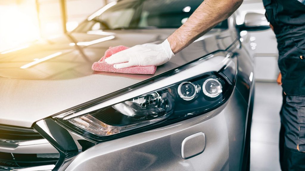 Expert en soins auto utilisant un spray commercial pour retirer la résine et sève séchée sur une voiture.